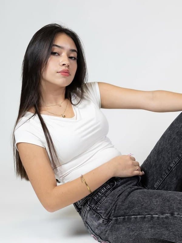 Eilin Guependo recostada en el suelo de un estudio, con camiseta blanca y vaqueros grises