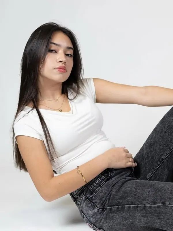 Eilin Guependo recostada en el suelo de un estudio, con camiseta blanca y vaqueros grises